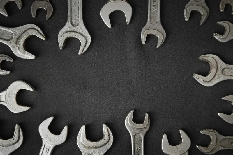 Open-ended metal wrenches of different sizes arranged in a circle on a dark grey background