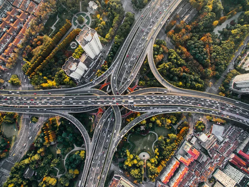 Aerial view of a large multi-level highway interchange in Shanghai with traffic flowing between green parks and apartment blocks