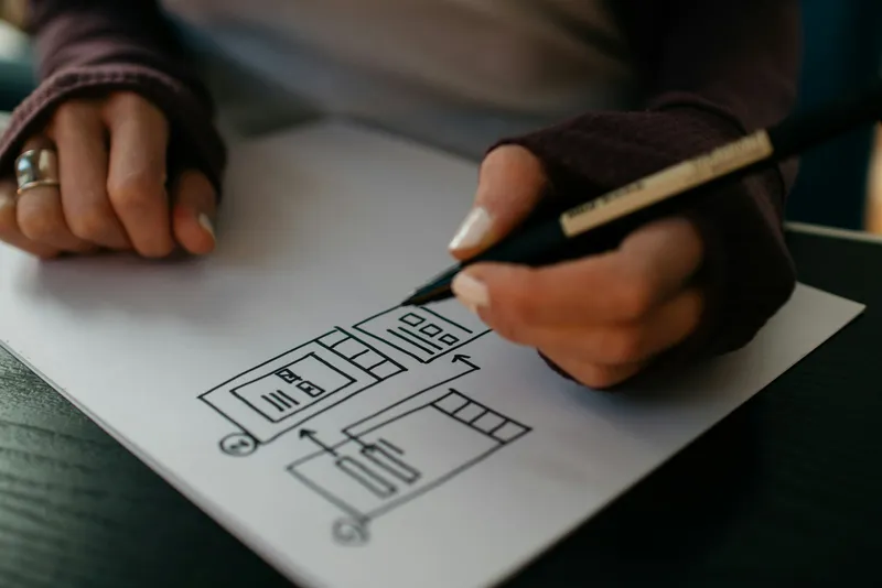 Close-up of a woman's hands drawing website wireframe sketches with a black marker on white paper