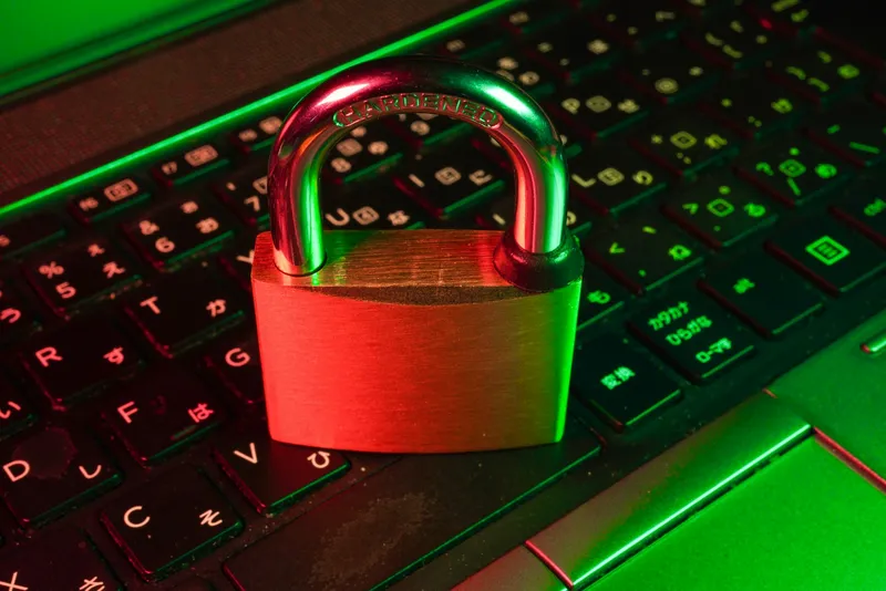 A brass padlock standing on a laptop keyboard, lit in red and green light